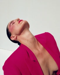 Close-up portrait of a woman in a magenta blazer with her head tilted back against a plain white background