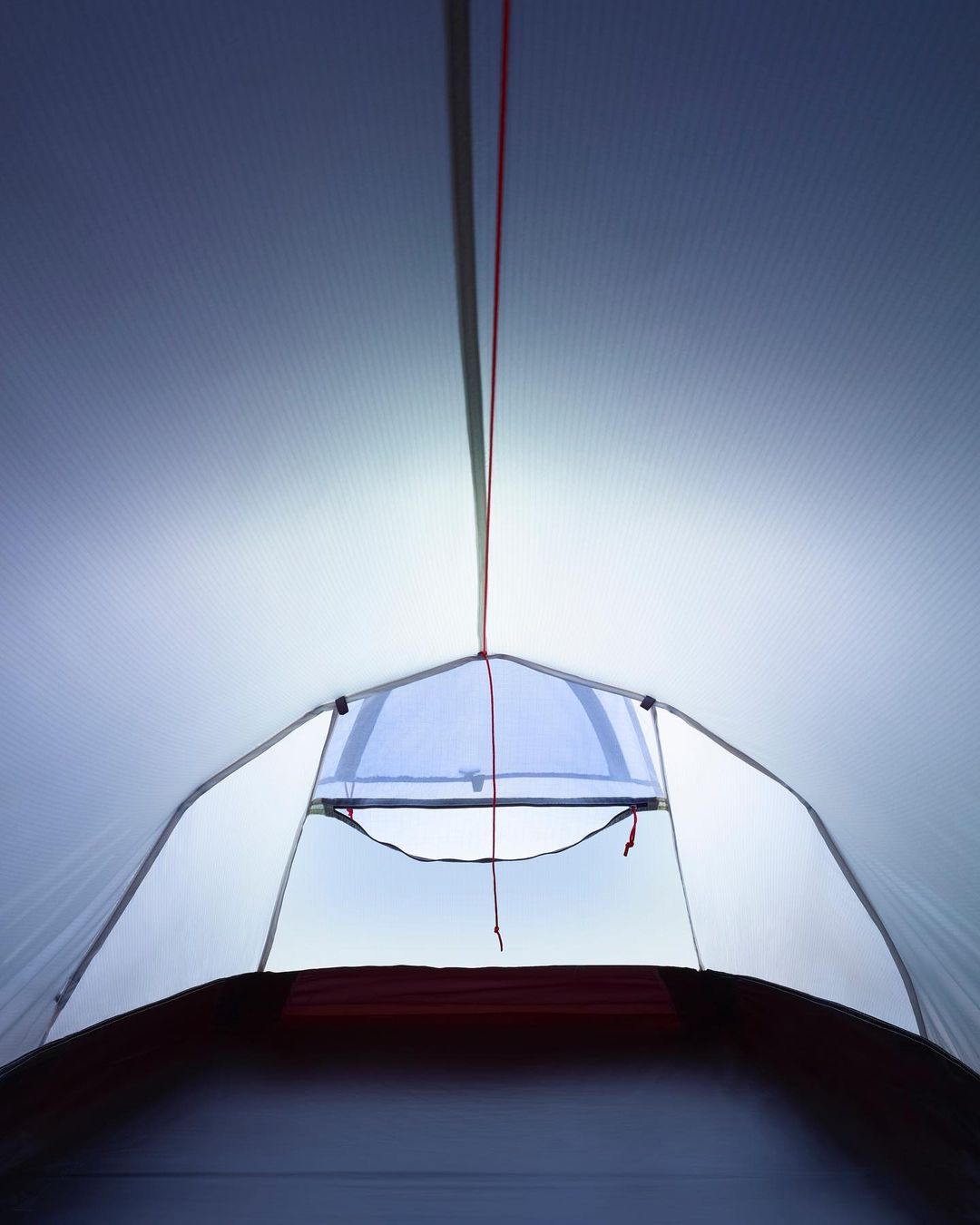 Interior view of a white camping tent with a window opening to the outdoors, showcasing camping equipment and outdoor recreation.