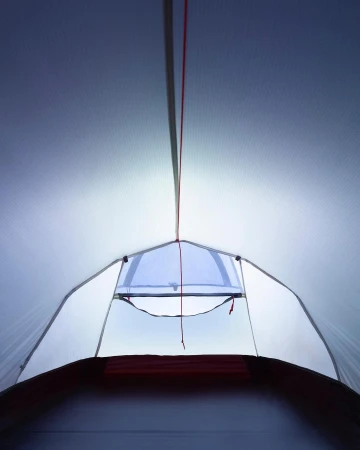Interior view of a white camping tent with a window opening to the outdoors, showcasing camping equipment and outdoor recreation.