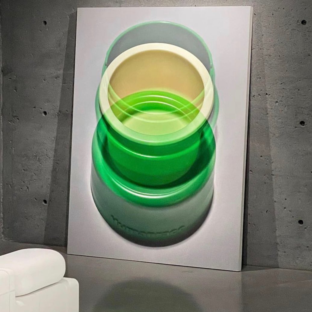 A green-and-cream colored abstract art print hangs on a gray wall, depicting overlapping green and cream bowls in a blurred style.