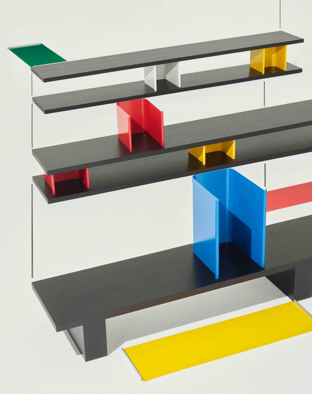 Abstract shot of a geometric design featuring black shelves and red, blue, green, and yellow vertical color blocks on a white background.