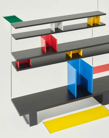 Abstract shot of a geometric design featuring black shelves and red, blue, green, and yellow vertical color blocks on a white background.