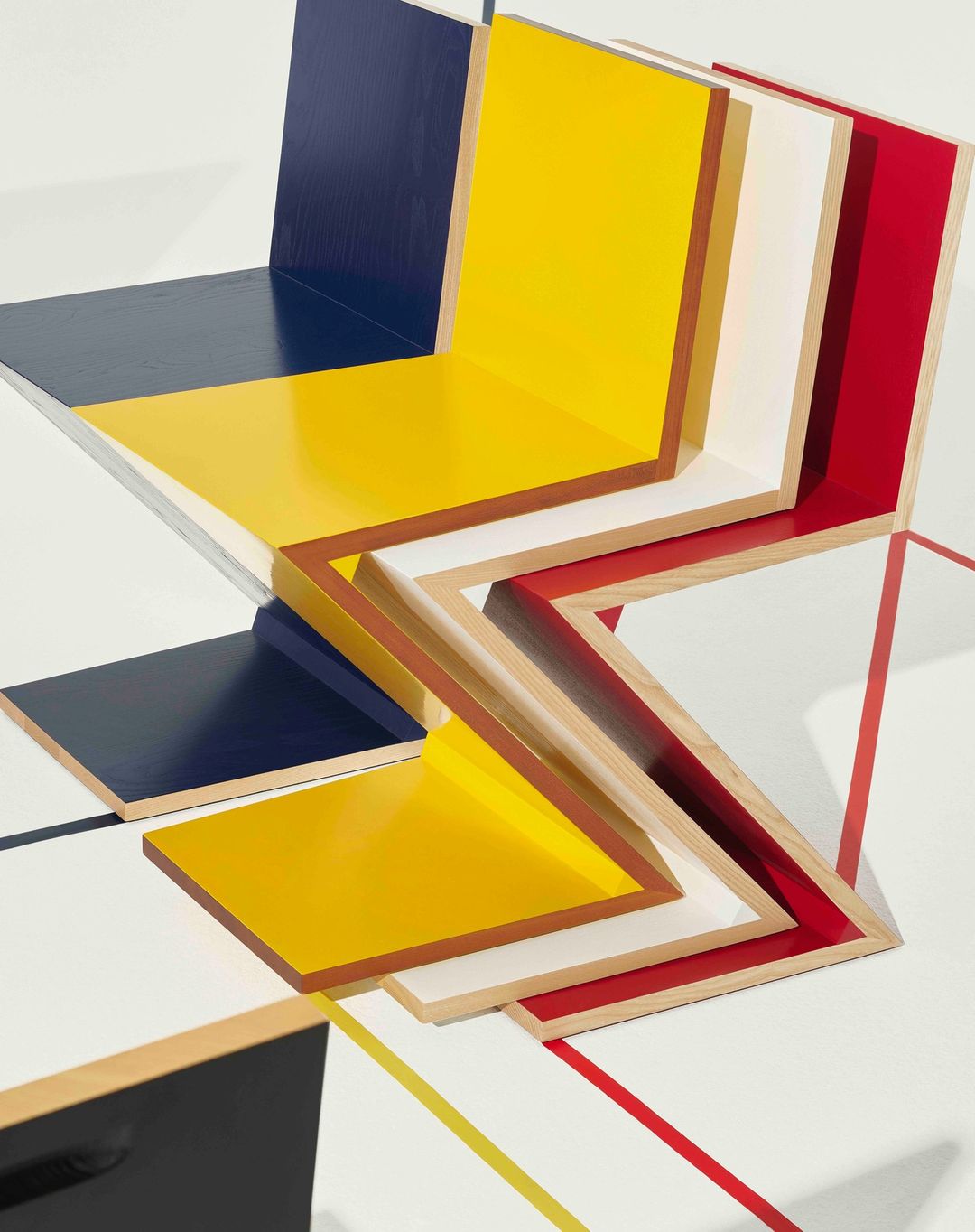 Abstract geometric composition with primary colors, wood frames, and a dynamic zig-zag pattern on a clean white background.