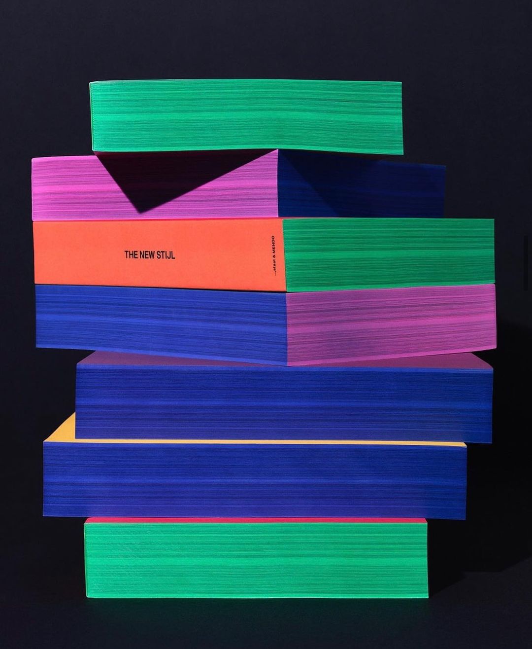 Stack of vibrant books in green, pink, orange, and blue against a dark background, creating a visually striking composition.