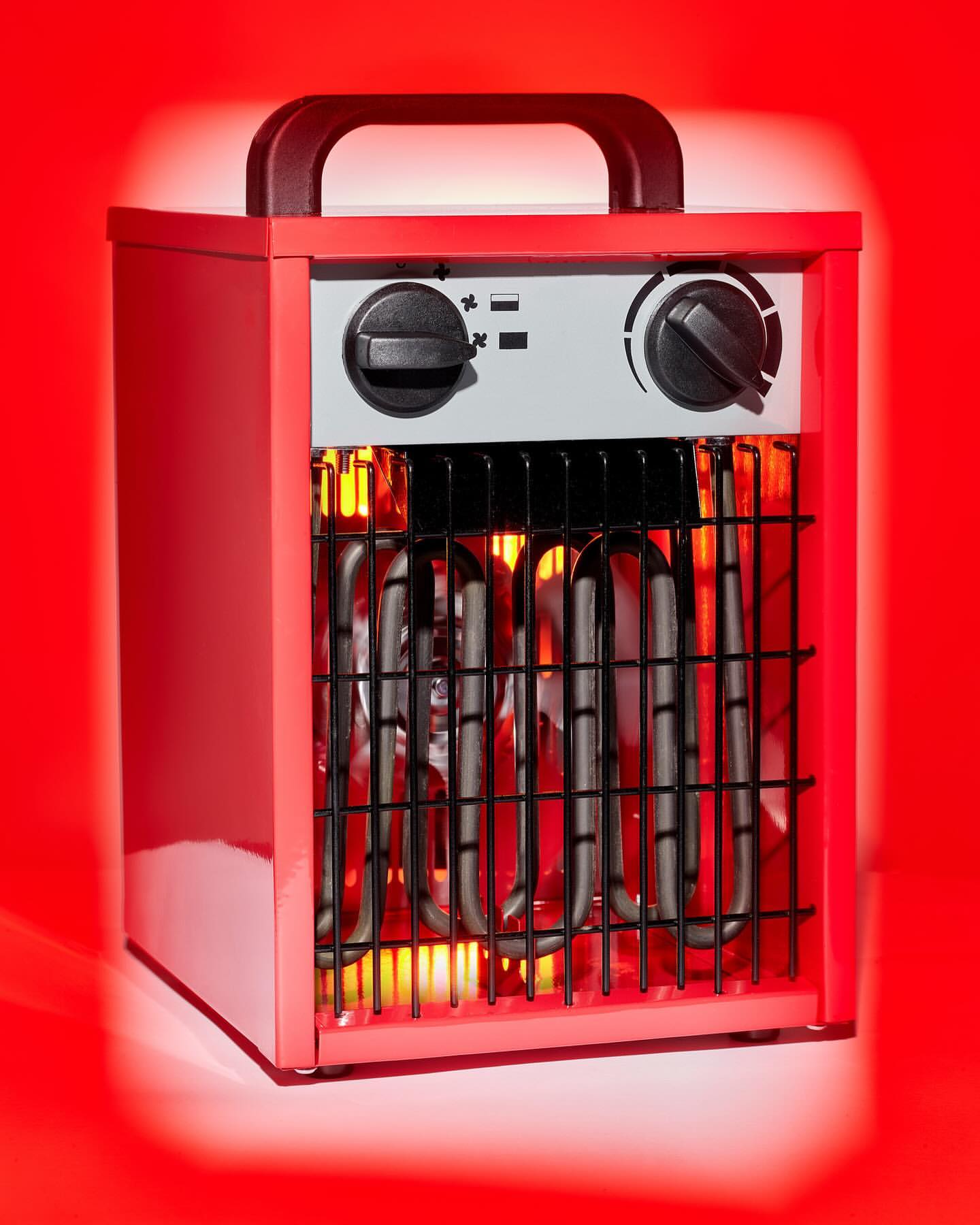 A red portable electric heater with black handle and controls stands against a red background, the heating elements glowing orange.