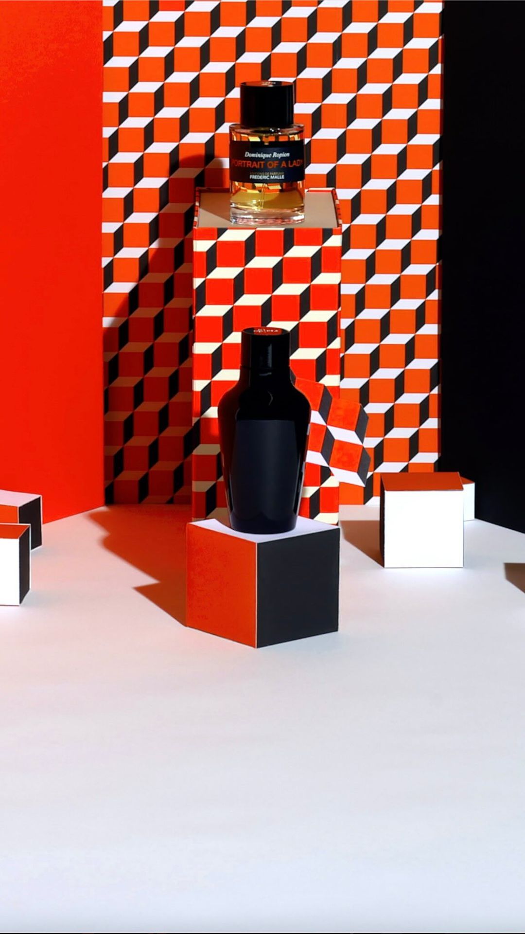 Still life shot of black and transparent perfume bottles placed on geometric blocks, with an orange and white pattern background.