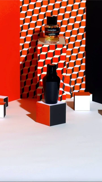 Still life shot of black and transparent perfume bottles placed on geometric blocks, with an orange and white pattern background.
