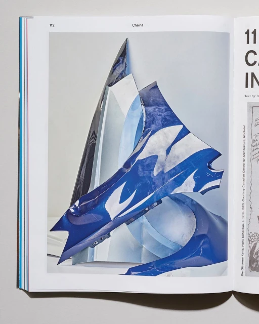 Abstract sculpture of blue and white shapes on the pages of an open book, displayed against a neutral studio backdrop.