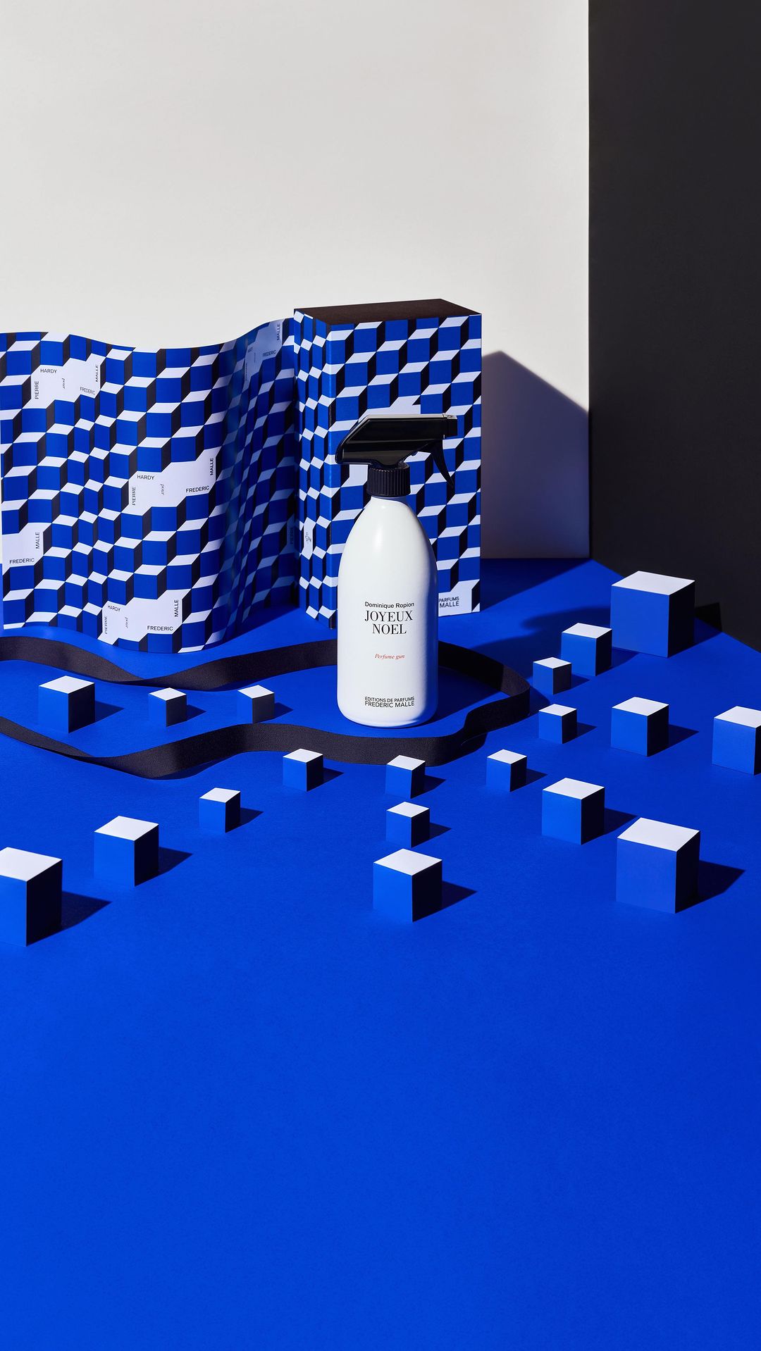 A spray bottle of cleaning fluid is staged on a blue surface with geometric paper and cube props, showcasing product photography.