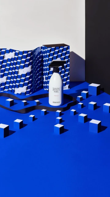 A spray bottle of cleaning fluid is staged on a blue surface with geometric paper and cube props, showcasing product photography.