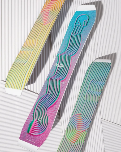 Three snowboards featuring colorful, geometric designs and the word 'Wallie' are displayed against a white background with striped shadows.