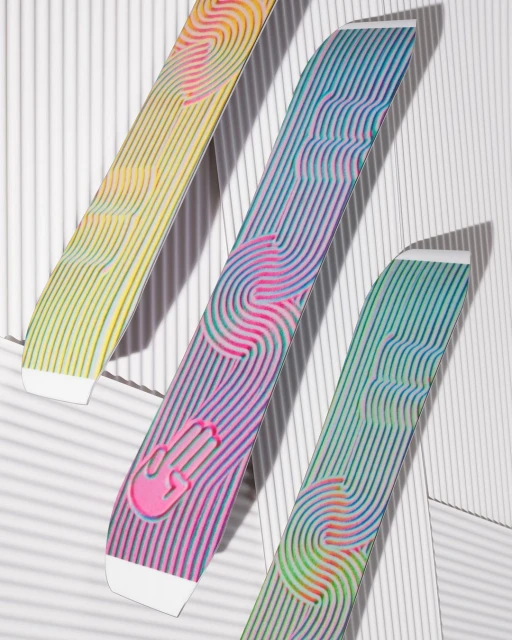 Three colorful snowboards are lined against a white wall, casting soft shadows and featuring a rainbow of hues and abstract designs.