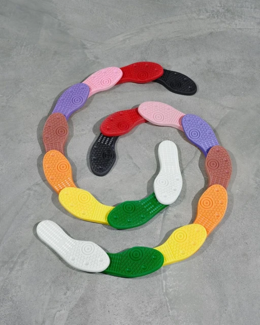 Colorful soles of shoes arranged in a spiral on a gray background, showcasing a spectrum of colors from white to black.