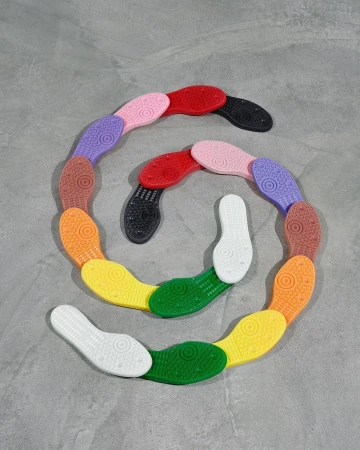 Colorful soles of shoes arranged in a spiral on a gray background, showcasing a spectrum of colors from white to black.