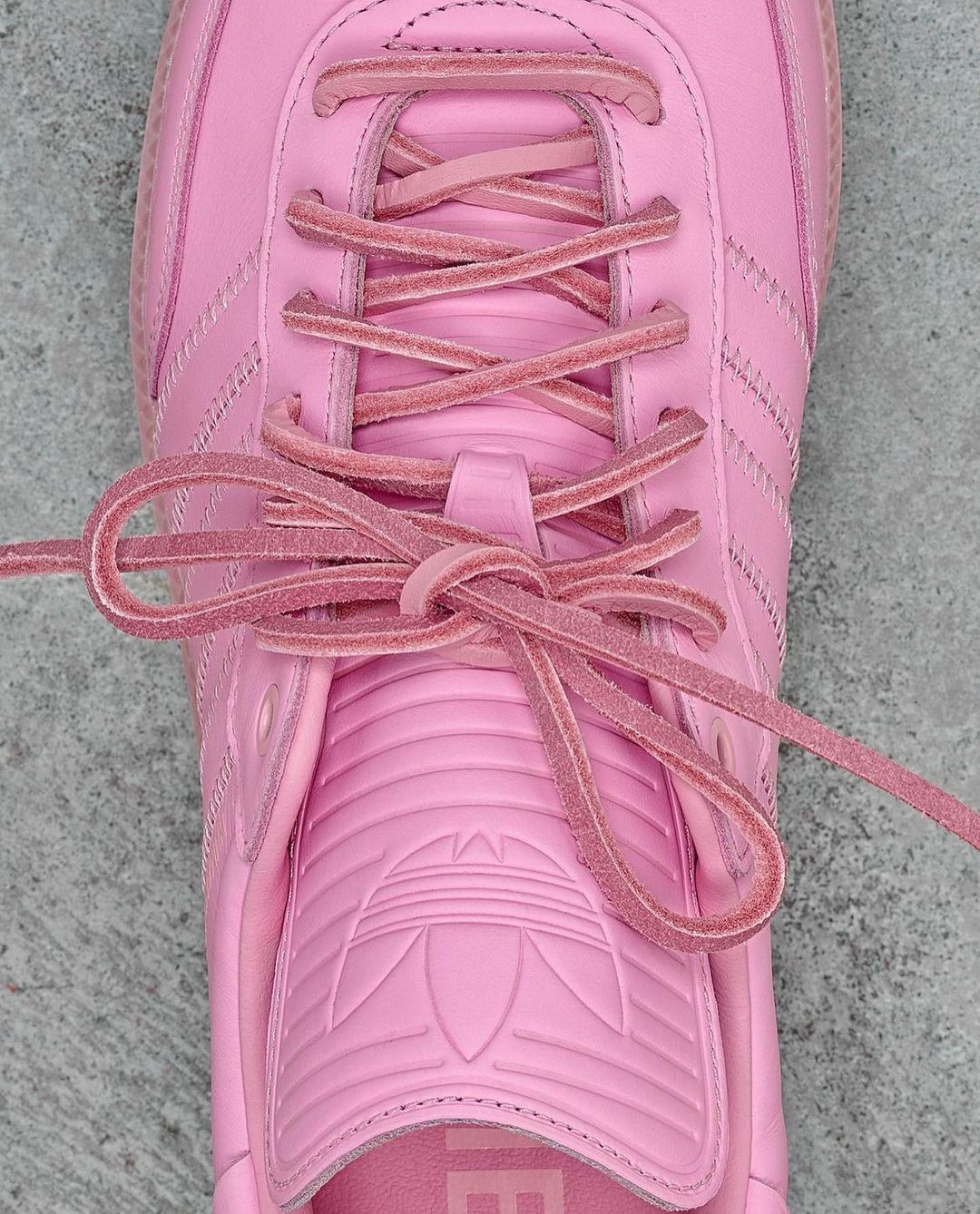 Close-up of a pink Adidas Samba shoe with matching laces tied. The shoe has the iconic three stripes and brand logo.