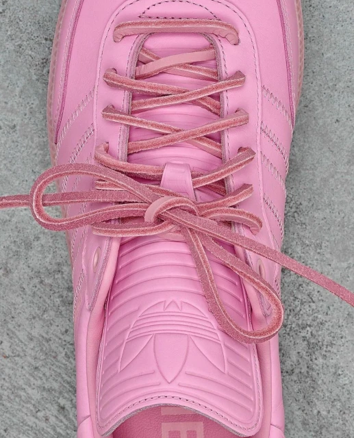 Close-up of a pink Adidas Samba shoe with matching laces tied. The shoe has the iconic three stripes and brand logo.
