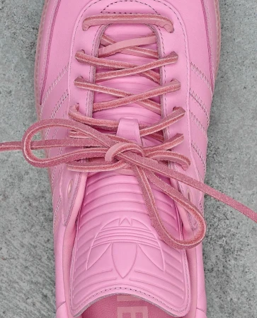 Close-up of a pink Adidas Samba shoe with matching laces tied. The shoe has the iconic three stripes and brand logo.