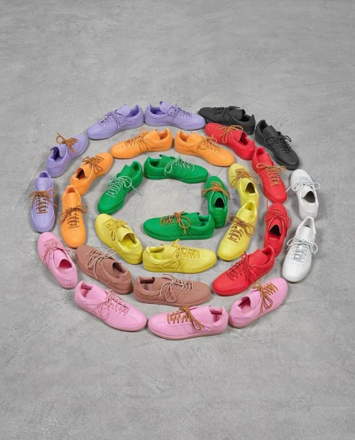 Overhead shot of colorful sneakers arranged in a spiral pattern on a textured grey surface, showcasing a spectrum of color and design.