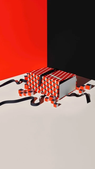 Geometric gift box with red and white pattern and black ribbon sits on a cream surface against a red and black corner backdrop.