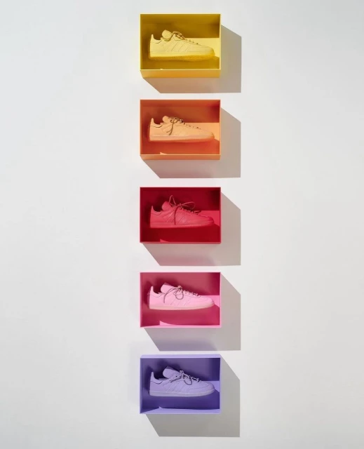 A row of five colourful boxes, each displaying a monotone sneaker in yellow, orange, red, pink, and purple, on a white background.