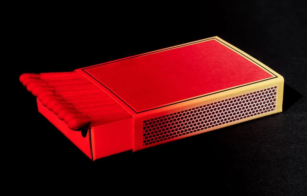 Still life of a box of red-tipped wooden matches partially open on a black background, side of box showing strike paper.