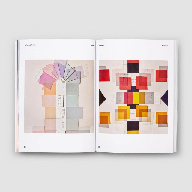 Open book displays colorful square paper compositions and design. One page features pastel color arrangement, while the other displays primary colors.