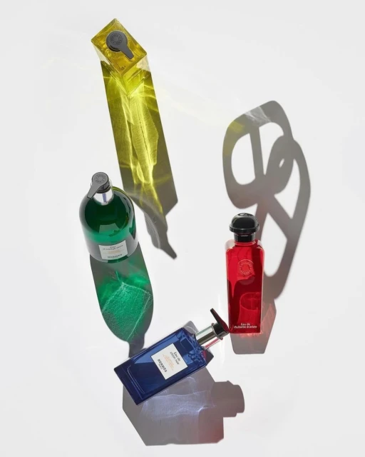 Four colorful glass bottles of perfume or body wash products are arranged on a white background with their shadows showing.