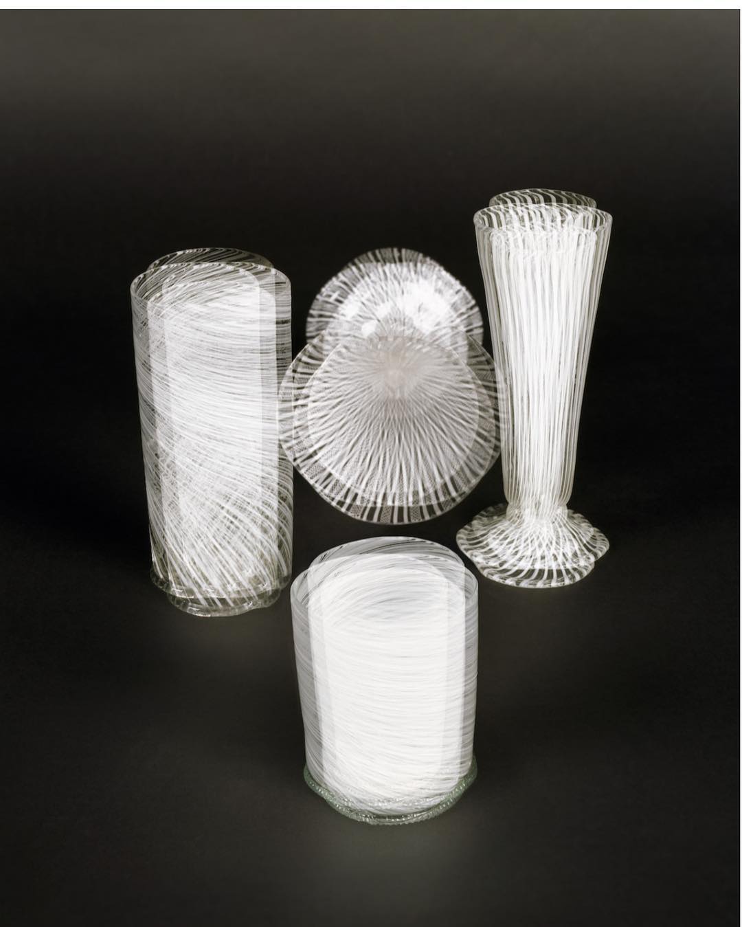 Several elegant clear glass vases and bowls are arranged against a dark background in a still life composition for product marketing.