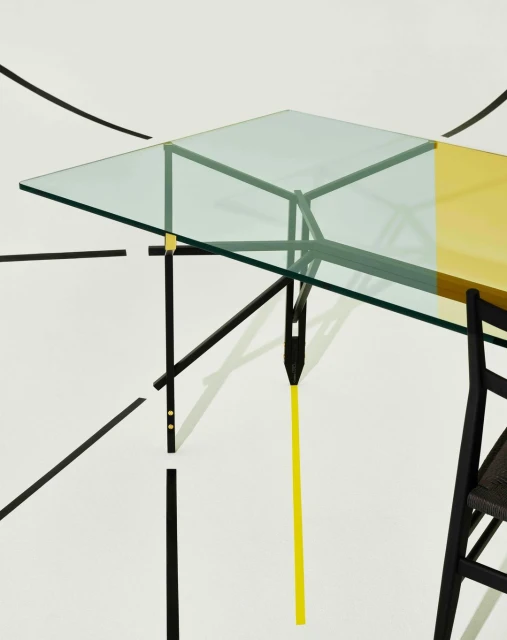 Modern interior featuring a glass-topped desk with black frame and yellow accents, paired with a black chair in a minimalist setting.