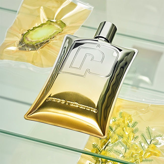 Shiny gold and silver perfume bottle with clear plastic sealed packs of plant cuttings on a clear glass shelf, studio lighting.