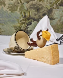 Surreal still life featuring a tipped teacup, a wedge of cheese, and an egg figure with arms and legs, photographed by Scheltens & Abbenes.