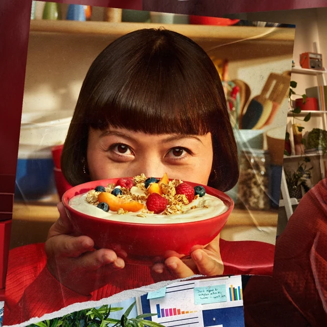 Eye-level image features a woman holding a red bowl of yogurt with fruit and granola, in front of a blurred interior background.