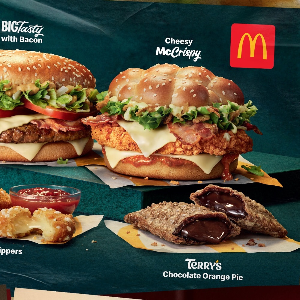 McDonald's sandwiches and desserts arranged on a display against a dark green background, including cheeseburgers, apple pies, and chicken.