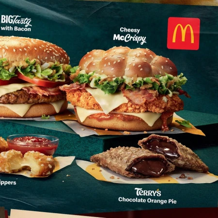 McDonald's sandwiches and desserts arranged on a display against a dark green background, including cheeseburgers, apple pies, and chicken.