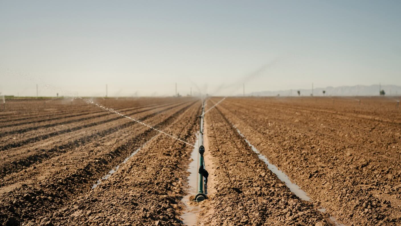 Irrigation system waters a cultivated field under a clear sky, showing agricultural technology and water resources management.
