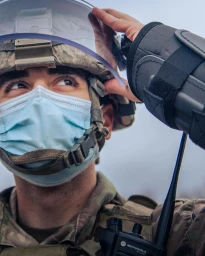 Close-up portrait of a law enforcement officer wearing a tactical helmet, face mask, and protective arm guard.