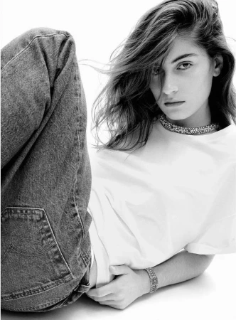 Monochrome portrait of a young woman with long wavy hair wearing a white t-shirt, jeans, and jeweled necklace and bracelet.