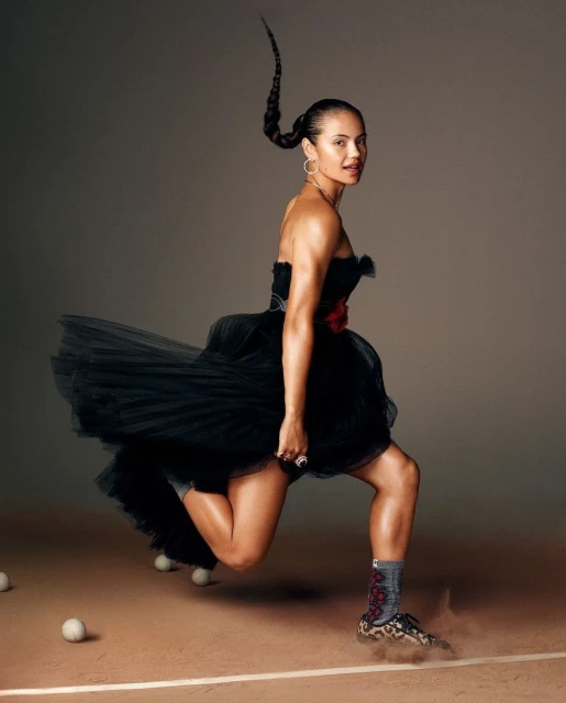 Athletic woman in a short black dress and sneakers running on a tennis court, against a neutral backdrop with scattered tennis balls.