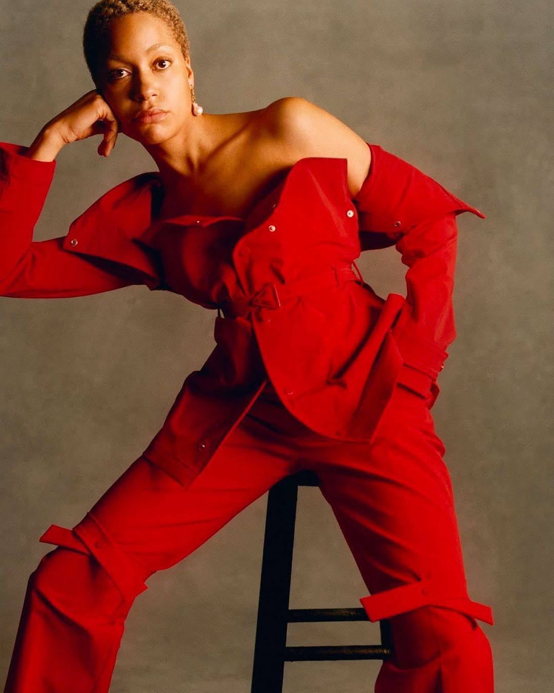 Elegant portrait of a woman with short hair in a striking red pantsuit striking a fashionable pose in front of a neutral backdrop.