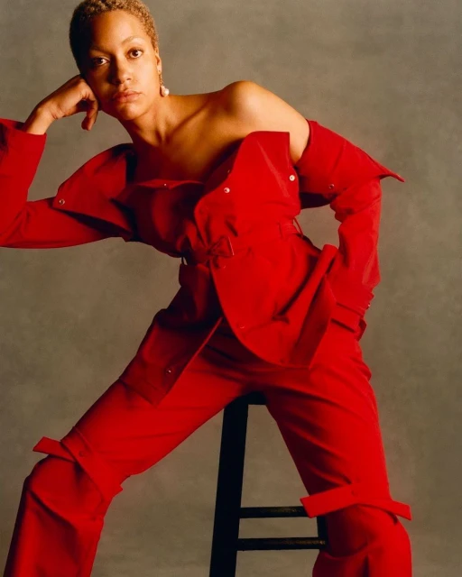 Elegant portrait of a woman with short hair in a striking red pantsuit striking a fashionable pose in front of a neutral backdrop.