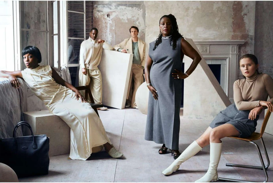 Group of five diverse fashion models in neutral-toned clothing in a bright indoor setting with props and painted backdrop.