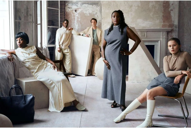 Group of five diverse fashion models in neutral-toned clothing in a bright indoor setting with props and painted backdrop.