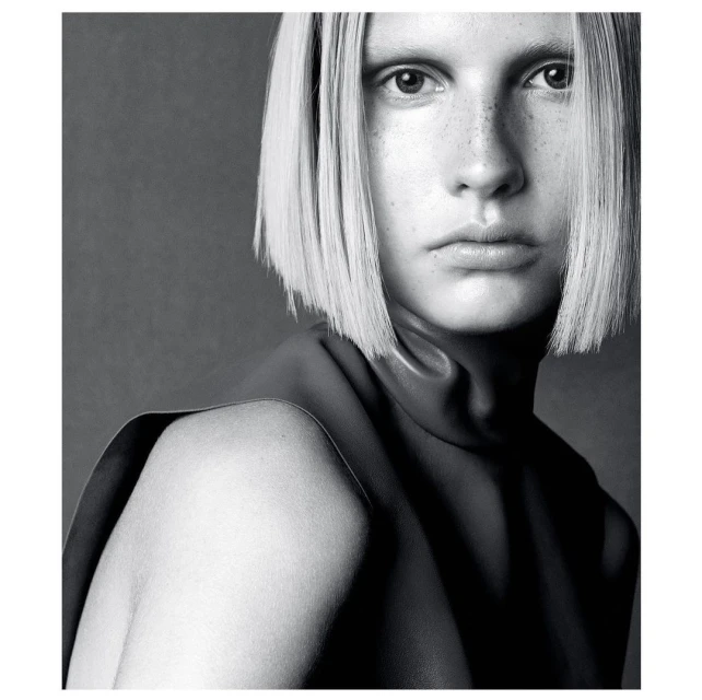 Portrait of a fair-skinned woman with a bob haircut posing in a sleeveless, leather top against a dark grey backdrop in a studio.