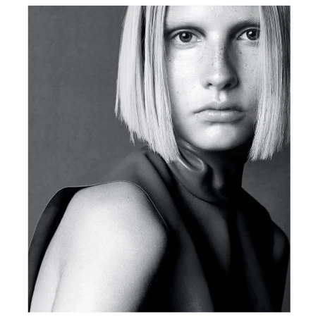 Portrait of a fair-skinned woman with a bob haircut posing in a sleeveless, leather top against a dark grey backdrop in a studio.