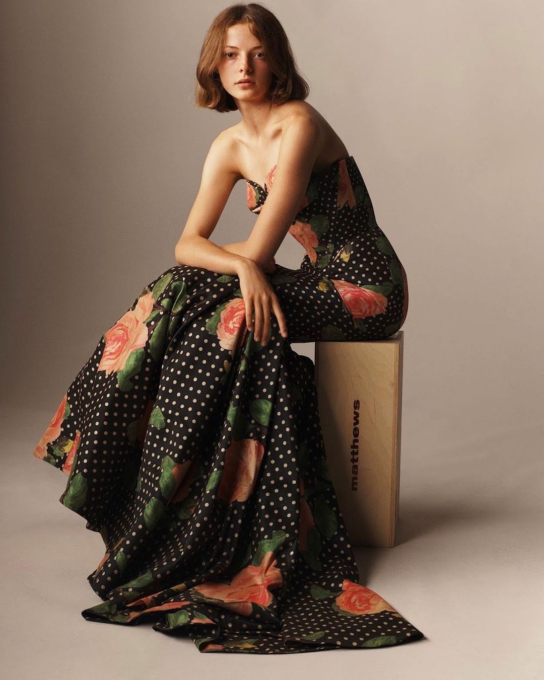 Model seated on wooden crate wearing strapless black gown with white polka dots and pink roses by Scott Trindle