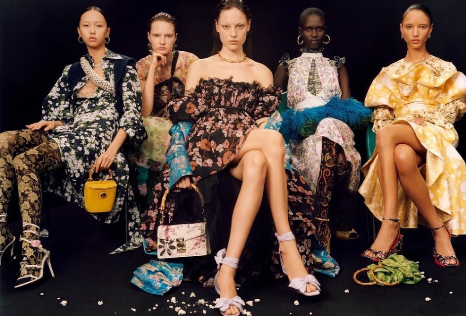 Five fashion models pose seated against a dark backdrop, showcasing floral print dresses, decorative tights, handbags, and stylish high heels.