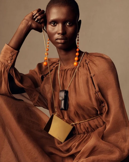 Dark-skinned woman in a brown dress poses in a close-up shot, adorned with orange beaded earrings and a crossbody bag on a neutral background.