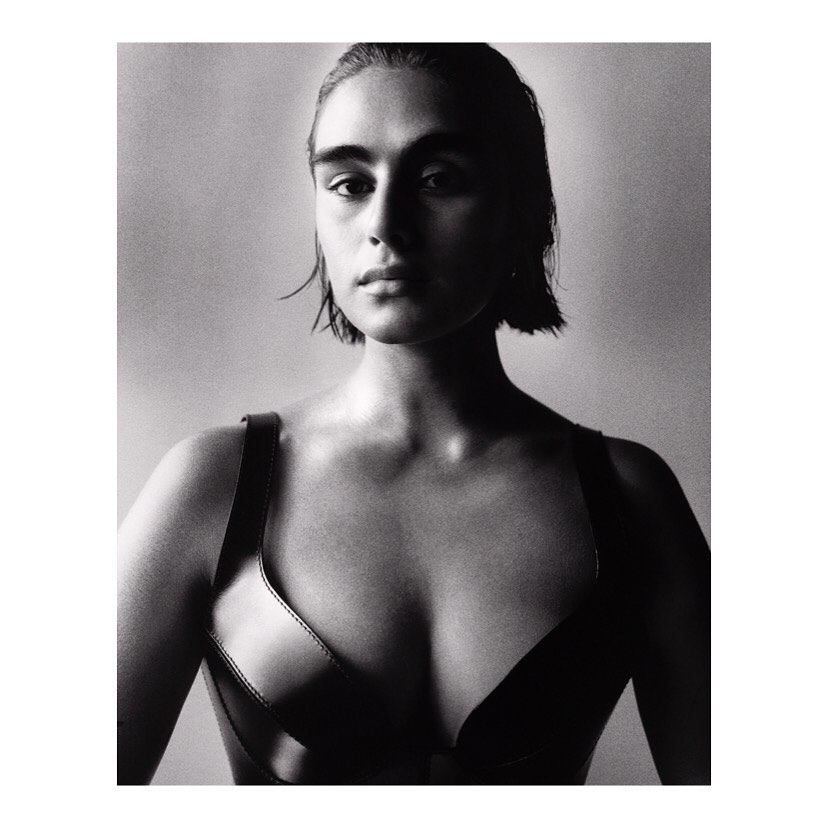 Monochrome portrait of a young adult woman with short, wet hair wearing a modern leather harness against a neutral background.