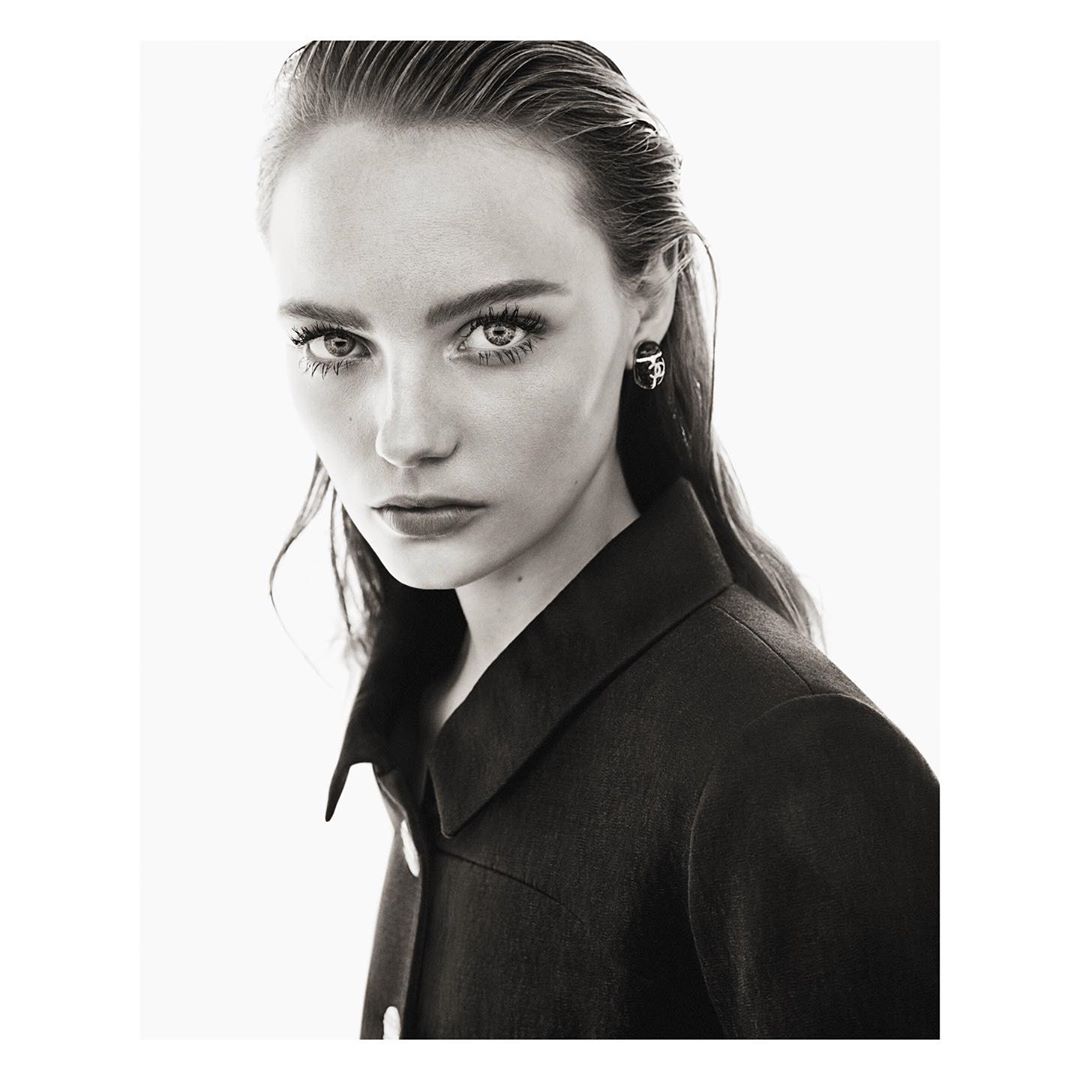 Close-up black-and-white portrait of a young woman with wet slicked-back hair, wearing a dark collared top against a white background.