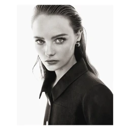 Close-up portrait of a woman with slicked-back dark hair wearing a dark collared jacket, captured in black and white.